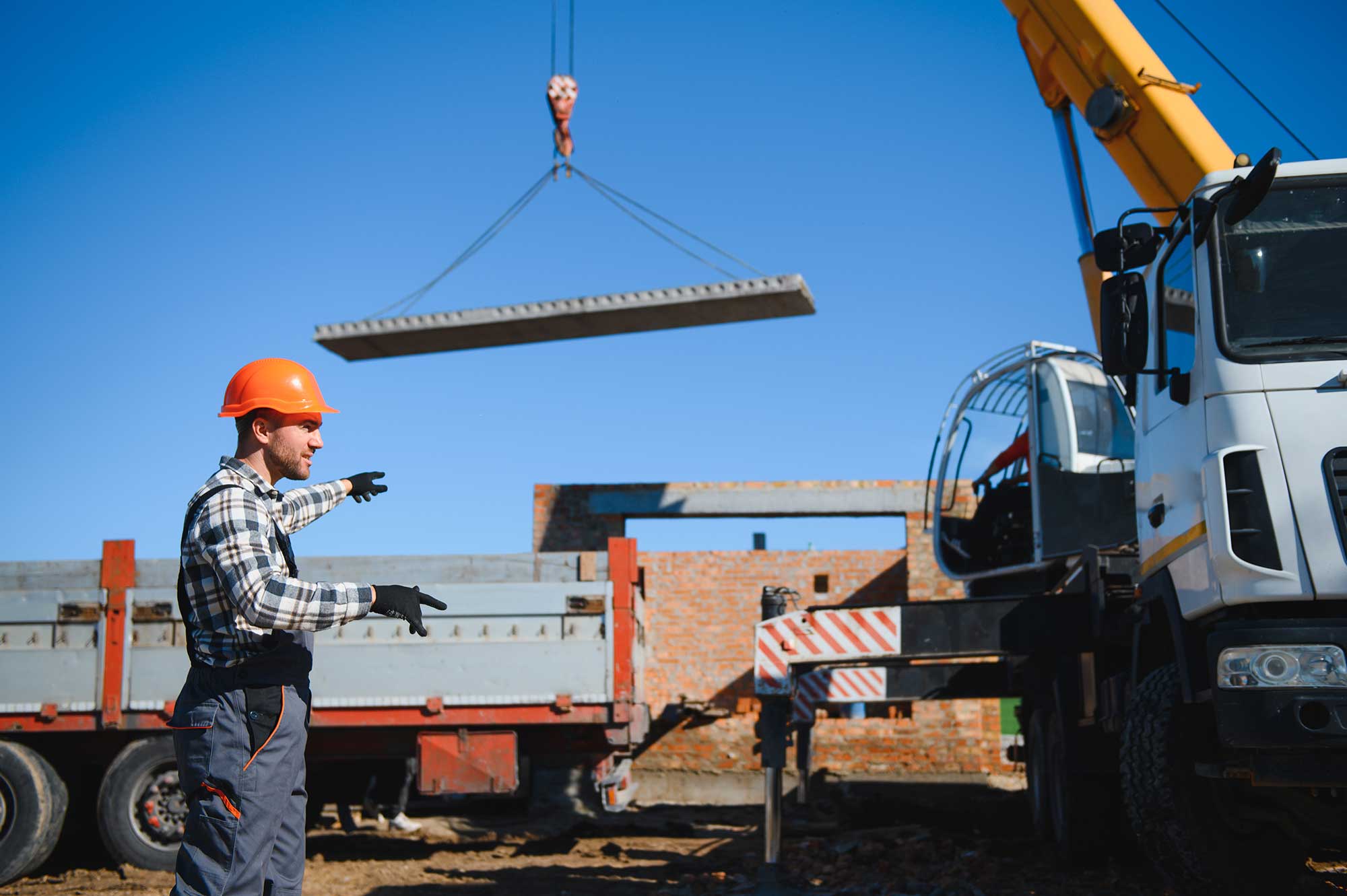 Crane lifting construction materials onto a flatbed trailer for on-site unloading.
