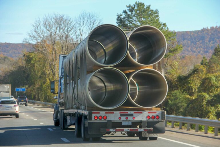 Flatbed truck loaded with oversized steel pipes for oilfield delivery.